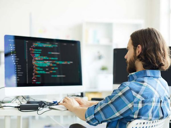 Serious pensive hipster young bearded coder in casual shirt creating computer software and working with desktop computer in modern office